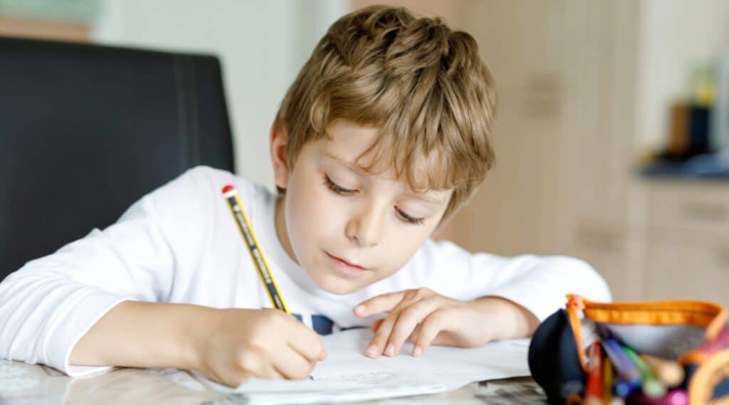 A young boy sitting at a table with pencil in hand. He is writing a story using story prompts.