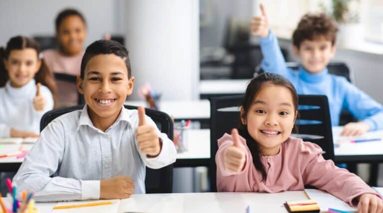 A group of elementary students sitting in class giving a thumbs up because they know it's time for grammar games.