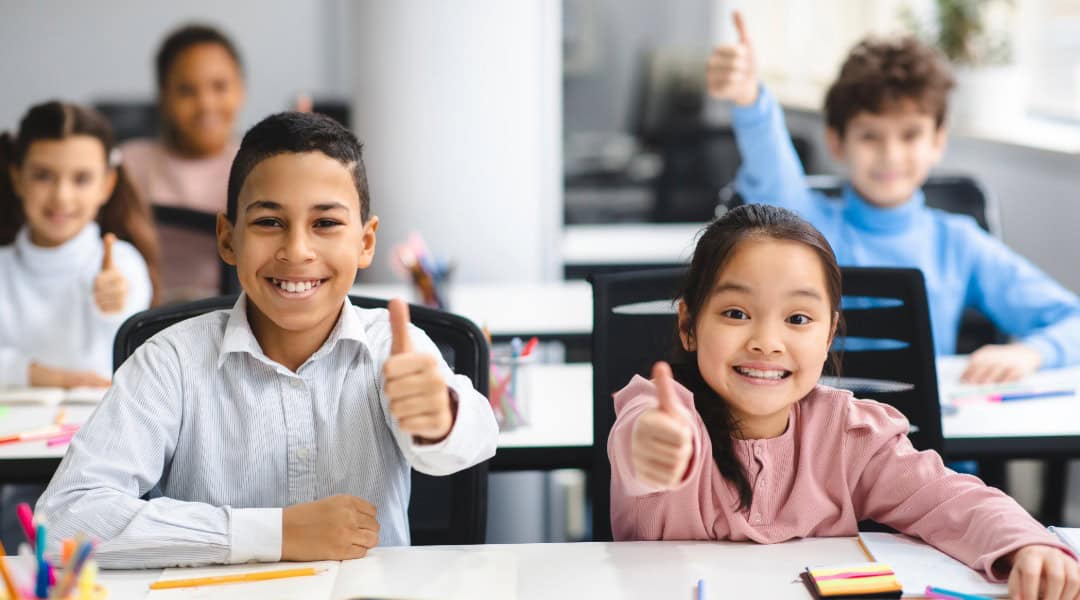 A group of elementary students sitting in class giving a thumbs up because they know it's time for grammar games.