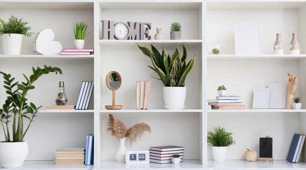 A picture of a nicely organized home book shelf with plants and small statues. White and modern looking. The perfect setting for a bunch of great parenting books!
