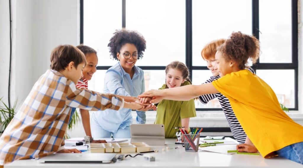 A teacher and four elementary students celebrating after solving a word association game riddle.