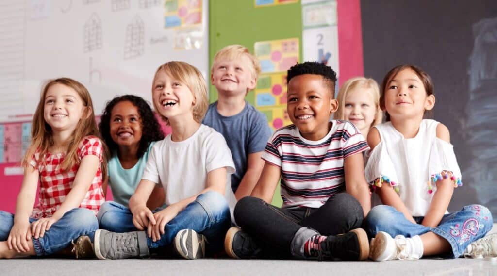 A group of elementary students sitting on the classroom floor excited for their Montessori great lesson.