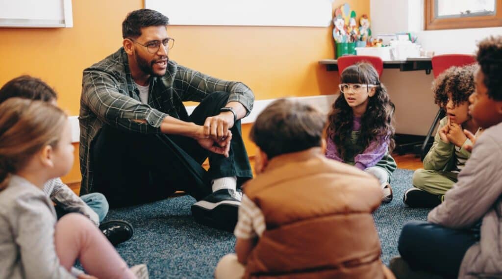 A group of students and a male teacher sitting on the floor going through some Montessori great lessons resources. 