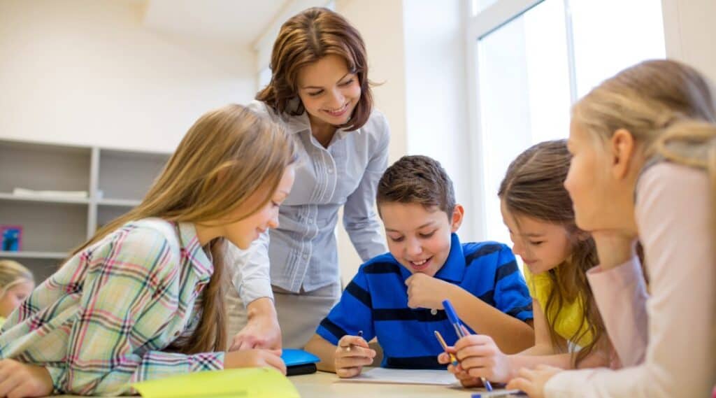 A small group of students and a teacher huddle around some Montessori great lessons resources.