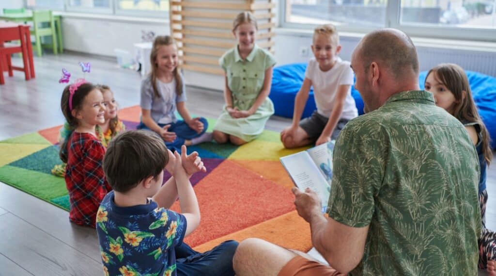 A group of students with their male teacher sitting on the floor looking through Montessori great lessons resources