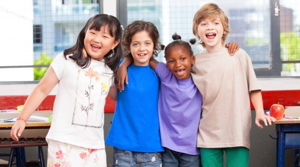 Four elementary aged children with their arms over each others shoulders, happy to be a school.