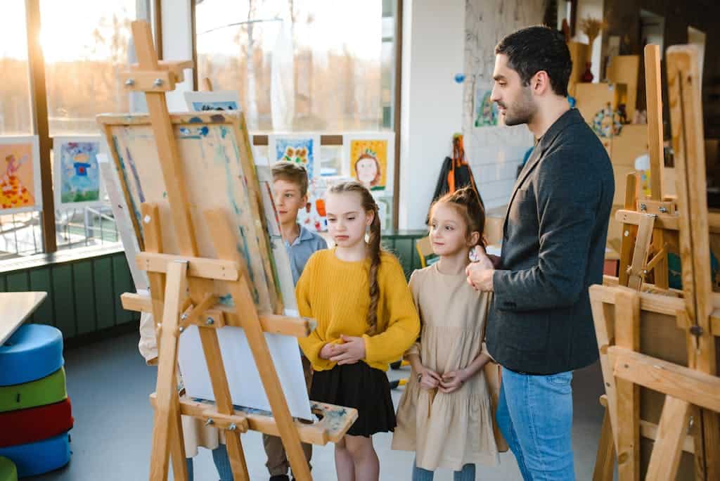 Children engaged in a grammar game under teacher's guidance, painting on easels.