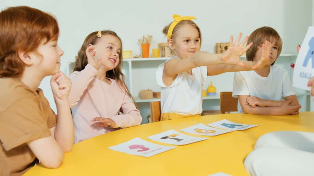 Happy kids engaging with alphabet cards around a yellow table in a fun classroom setting.