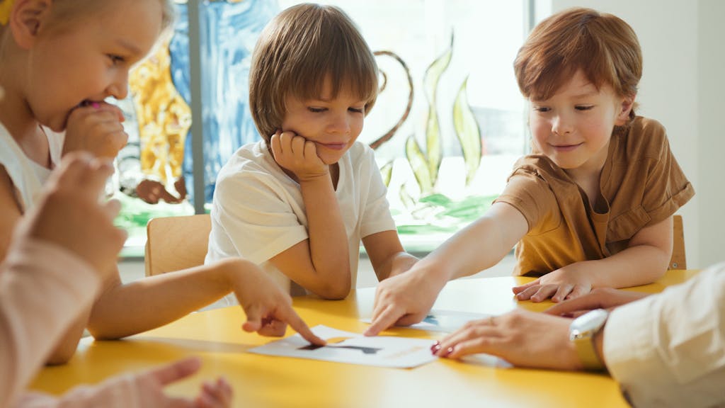 Young children engaging in fun learning activities at a yellow table in a classroom setting.