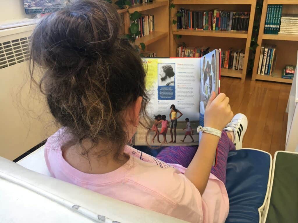 A picture of a grade 5 student reading a book in the reading area of the classroom. Students can choose what they want to do which I see as a plus for are Montessori schools good.