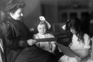 A black and white picture of Maria Montessori working with two school girls.