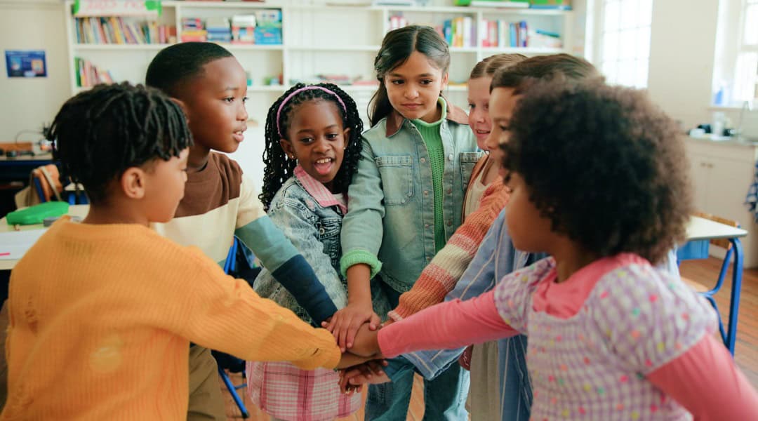 A group of students in the Montessori second plane of development putting their hands together for a cheer.
