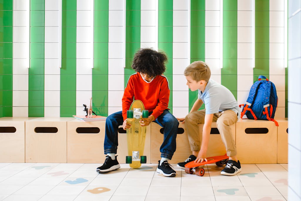 Two boys with skateboards sit indoors, engaging in conversation.