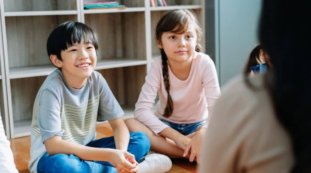 Two elementary students listening to their teacher, both looking happy.