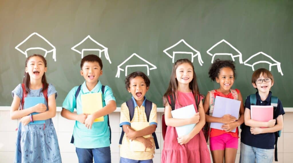 A picture of 6 elementary graduates standing in front of a chalkboard. On the chalkboard each student has a graduation cap drawn above their head.
