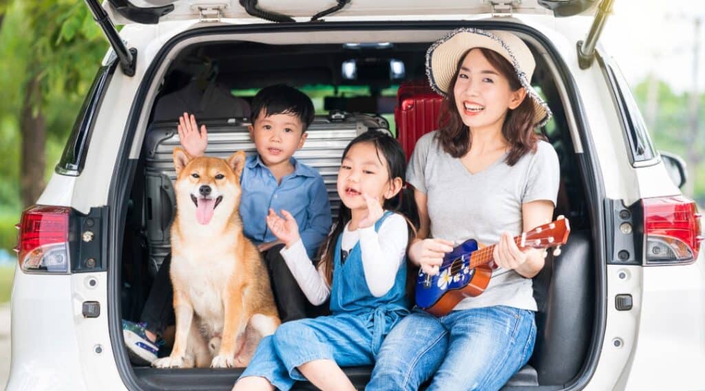 A mom and her two kids sitting in the trunk of their car signing a song as an activity to do on a road trip.