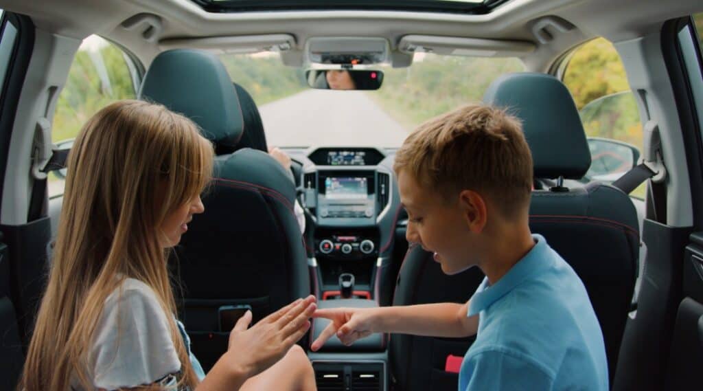 A brother and sister in the back seat of a car playing rock paper scissors. This is a classic and one of may favorite games to play on road trips.