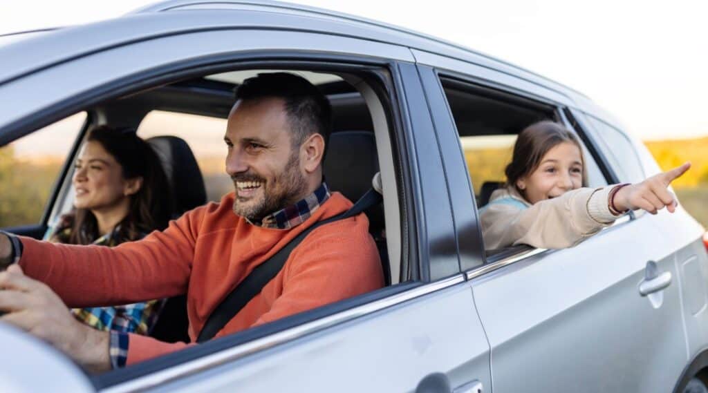 A family driving and the daughter pointing at something out the window.