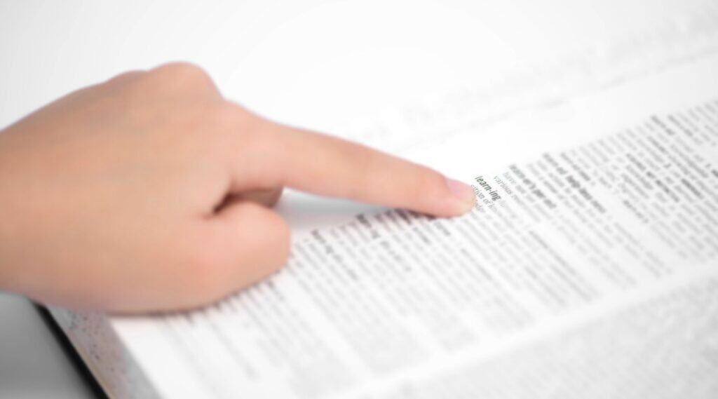 A picture of a finger scanning a dictionary. The student is looking for the word of the week.