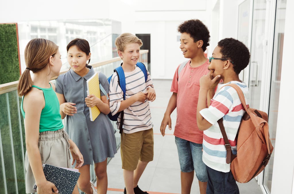Diverse group of students talking and laughing in a school hallway, holding books and bags. Their ability to communicate is heightened by the addition of a word of the week for students.