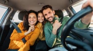 A mom and dad and daughter posing in the car before they head off on a road trip.