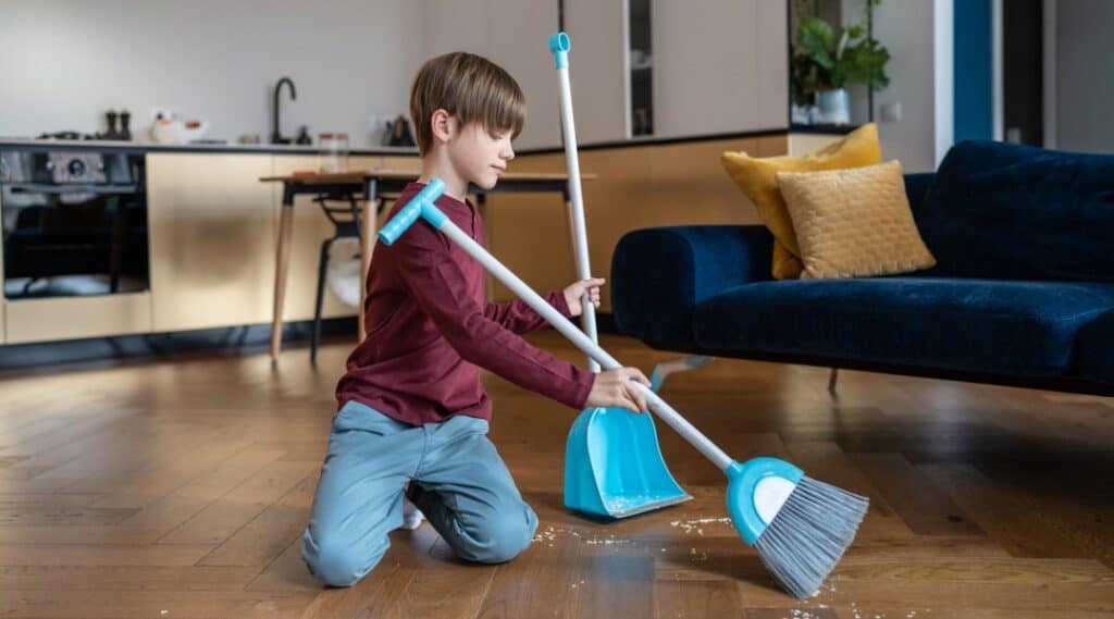Young child sweeping up after an activity to build practical life skills.