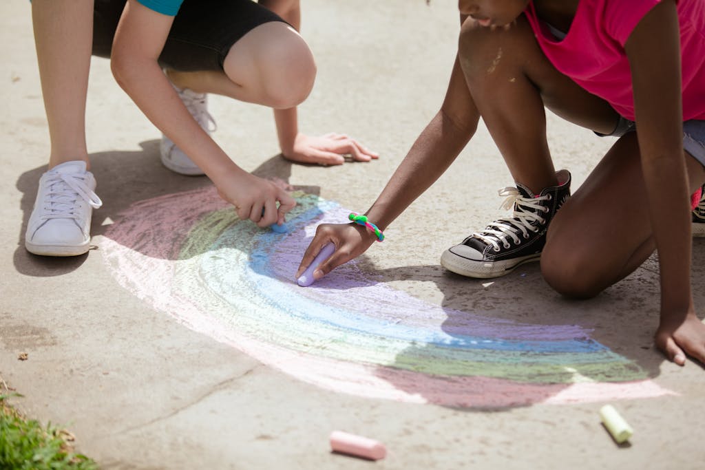 Kids having fun drawing a rainbow with chalk on the pavement in a park. This is always a popular choice for Montessori summer activities